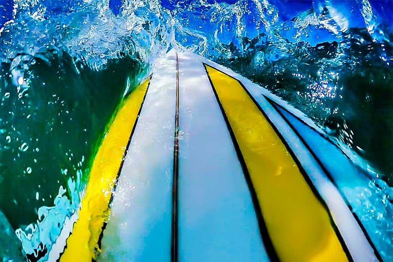 A man stands on a rock by the ocean, gazing at the waves under a clear blue sky.