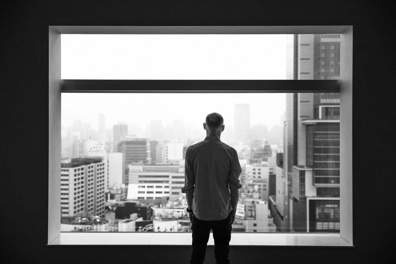 Photograph of a person looking out through a window of a skyscraper over a city of skyscrapers