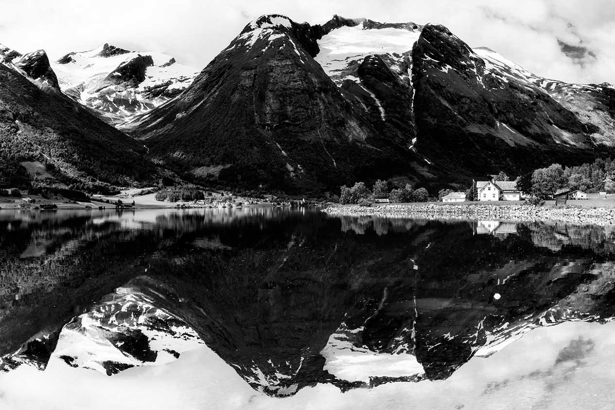 Snow-capped mountain with houses at its base, reflected in a lake in the foreground