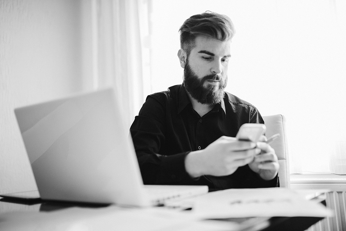 Uomo guarda un telefono davanti ad un computer aperto
