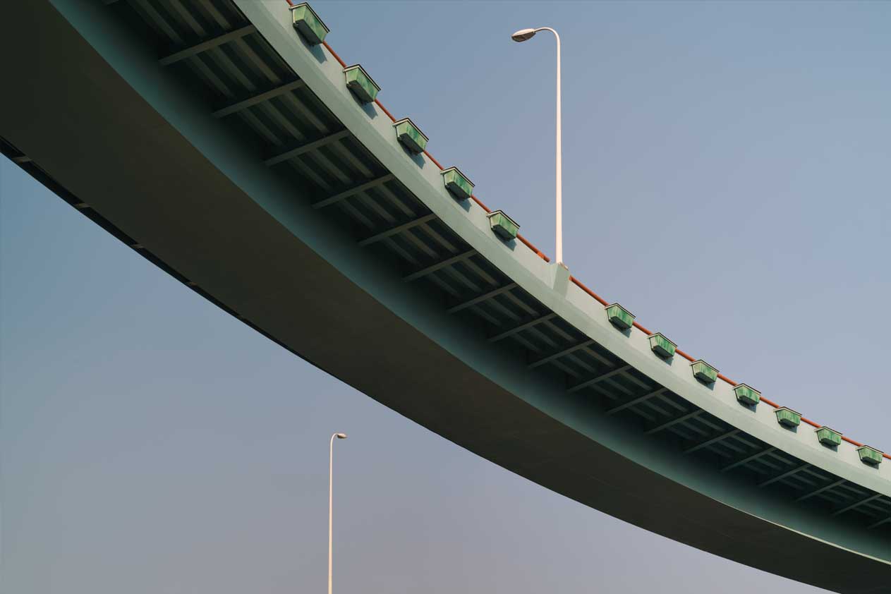 Sottostruttura curva di una strada sopraelevata con lampioni, contro un cielo limpido.