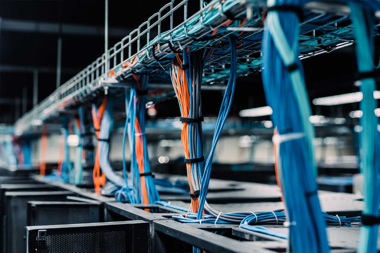 Gebundelde netwerkkabels geordend langs bovenliggende rekken in een datacenter, met blauwe en oranje bedrading in groepen vastgezet.