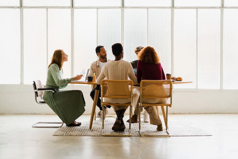 Group of professionals seated around a table in a bright meeting space, collaborating and discussing documents.