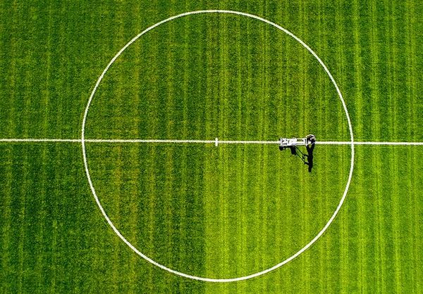 Aerial overhead view of a groundskeeper line-marking the centre circle of a lush green football pitch.