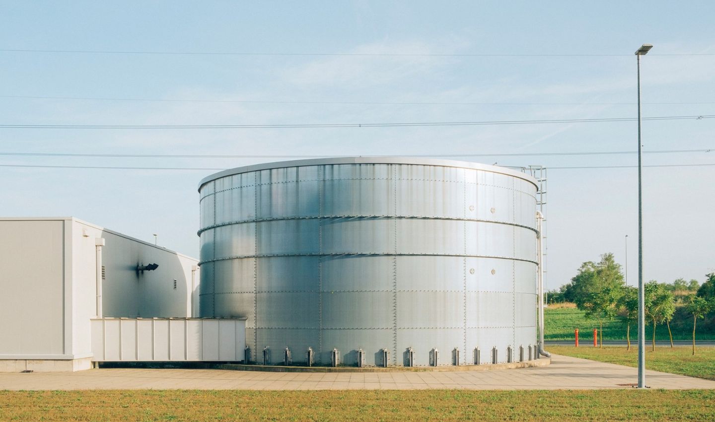 Large industrial storage tank beside a facility building with surrounding green landscape under a clear sky.
