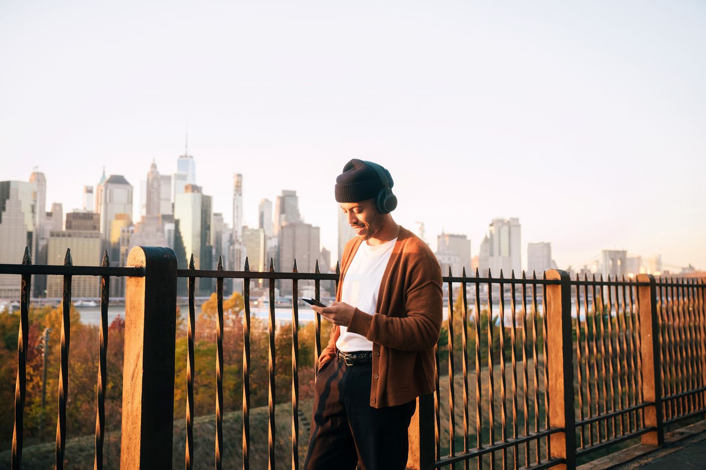 Man walking in front of Manhattan skyline, wearing a knit cap and headphones and smiling at smartphone. BlackRock; iShares; Portrait; individual investor