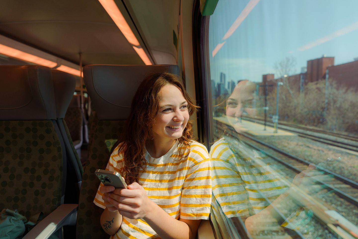 Happy woman using a smartphone and looking out of a train window. BlackRock; iShares; Portrait; individual investor